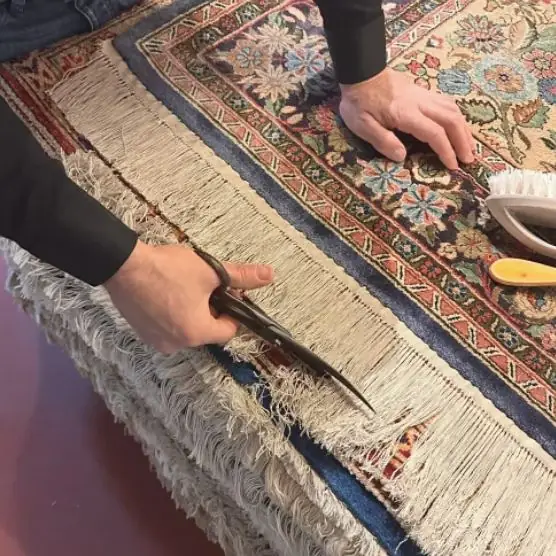 Artisan égalisant aux ciseaux la longueur des franges d'un tapis d'Orient