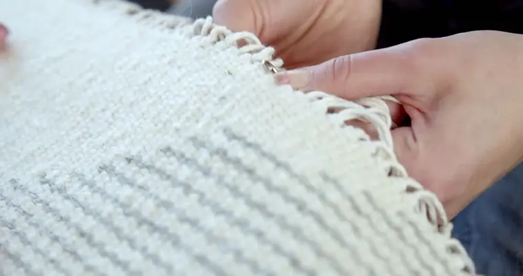 Mains vérifiant la régularité des franges neuves d'un tapis clair