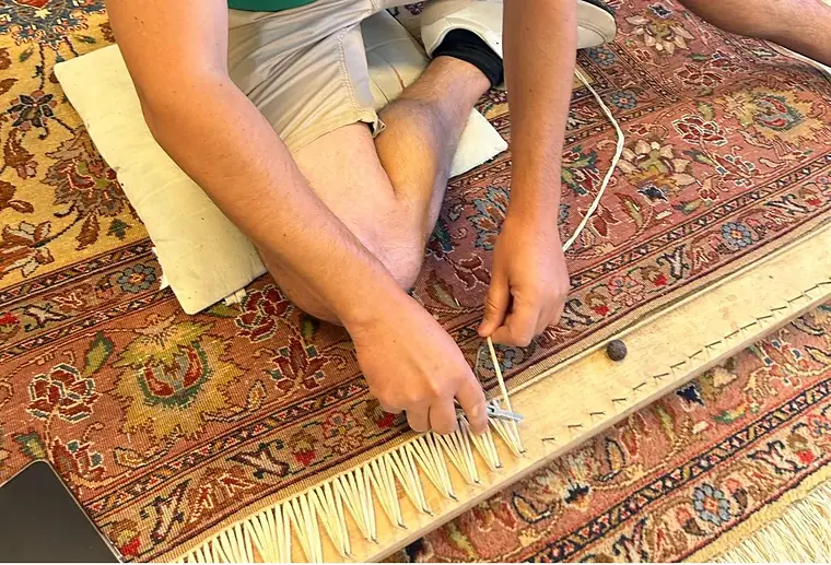 Artisan nouant les franges d'un tapis d'Orient à même le sol de l'atelier