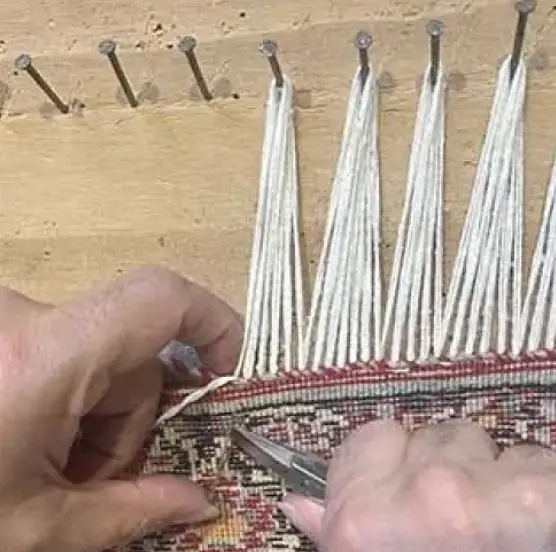 Franges de coton tendues sur un établi à clous pendant la réfection d'un tapis