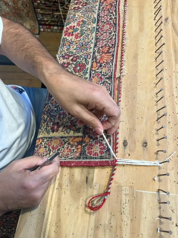 Mains nouant une à une les franges de coton neuves sur un tapis d'Orient