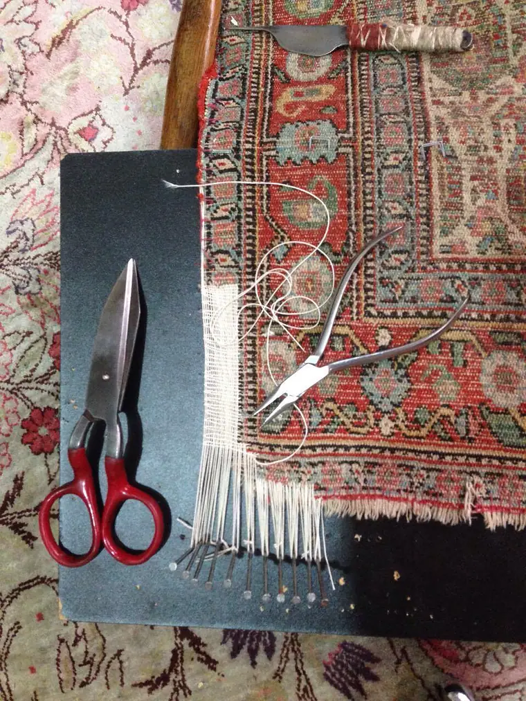 Ciseaux et aiguilles posés sur un tapis dont les franges sont en cours de réfection