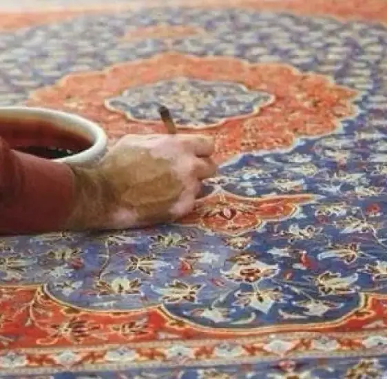 Artisan appliquant au pinceau une teinture sur le médaillon d'un tapis persan
