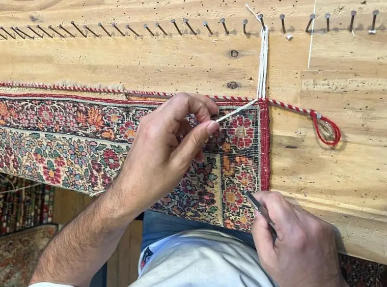 Artisan nouant des franges neuves sur la tête d'un tapis fixée à l'établi
