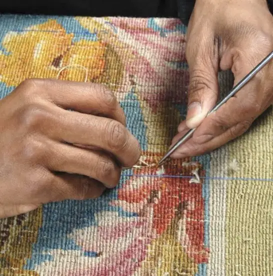 Mains d'artisan retissant à l'aiguille le motif floral d'un tapis ancien