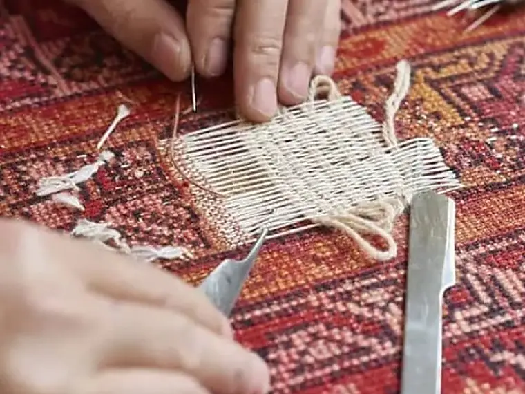 Mains reconstruisant la trame d'un trou dans un tapis d'Orient à l'aide d'un outil fin
